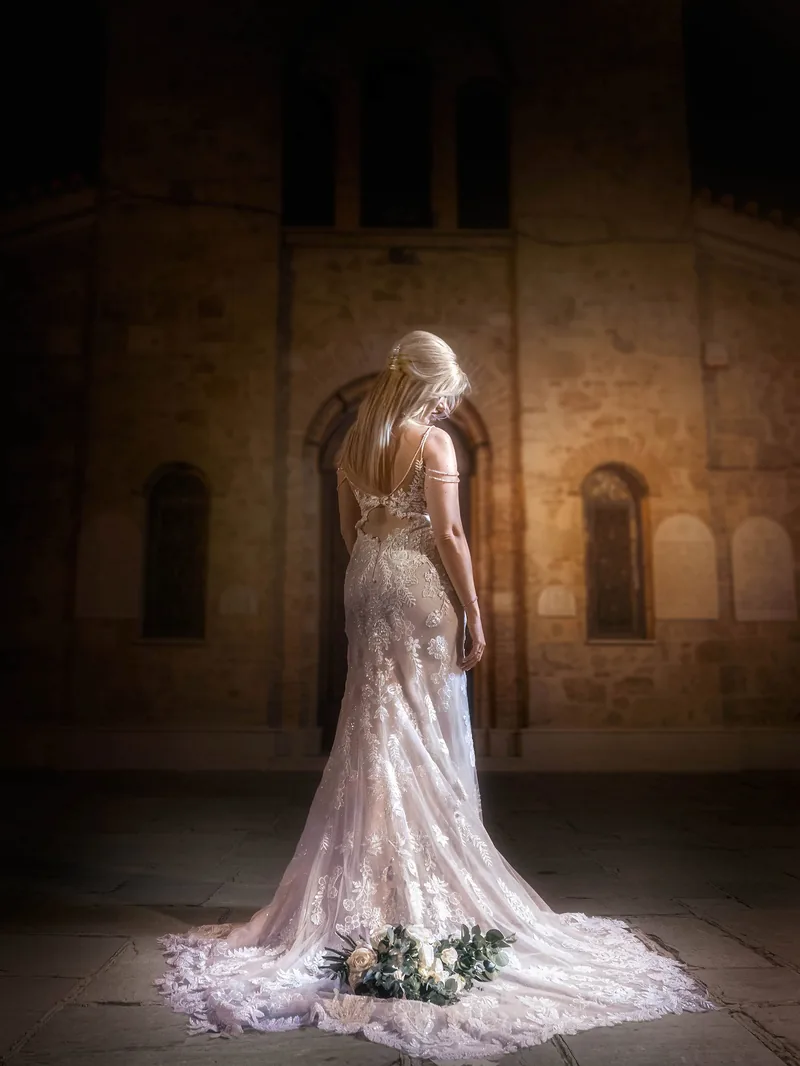 Νύφη με μακρύ νυφικό μπροστά σε πέτρινη εκκλησία