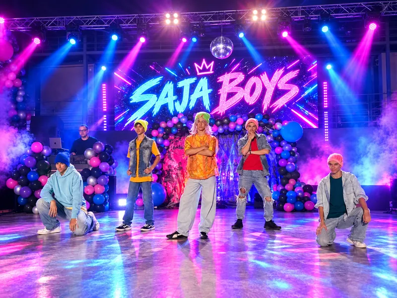 Οι Saja Boys ποζάρουν σε σκηνή με neon επιγραφή