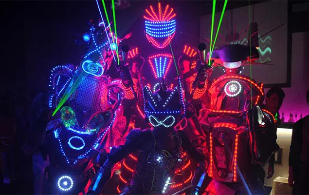 Performers με στολές LED και φωτεινά κοστούμια σε σκοτεινή σκηνή με laser